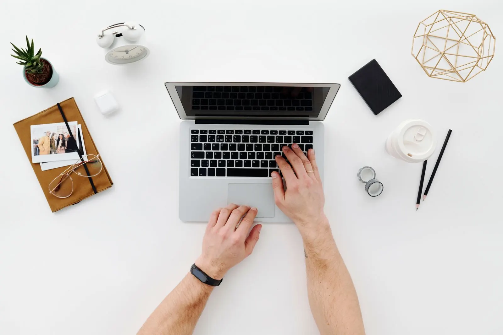 Hands at a laptop on a bright desk with notebooks and office supplies.